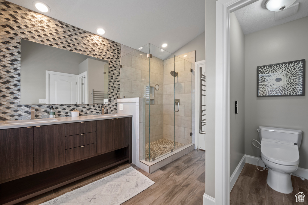 Bathroom featuring wood finished floors, a shower stall, double vanity, toilet, and baseboards