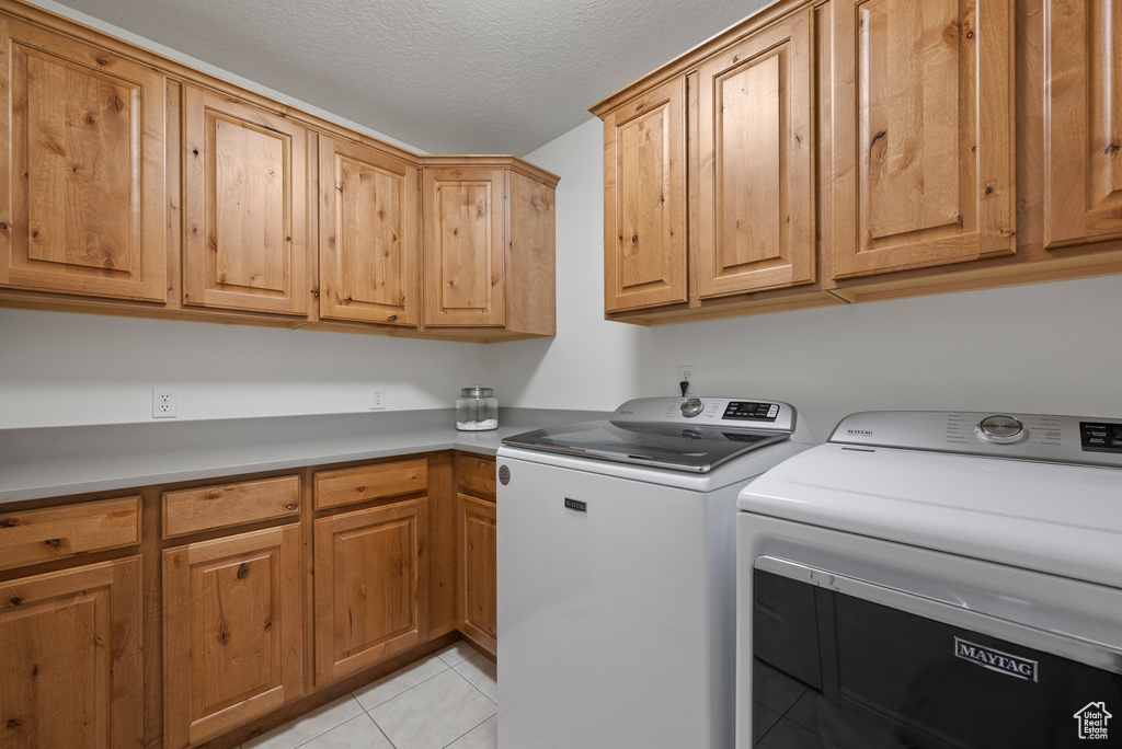 Washroom featuring cabinet space, washer and clothes dryer, light tile patterned flooring, and a textured ceiling