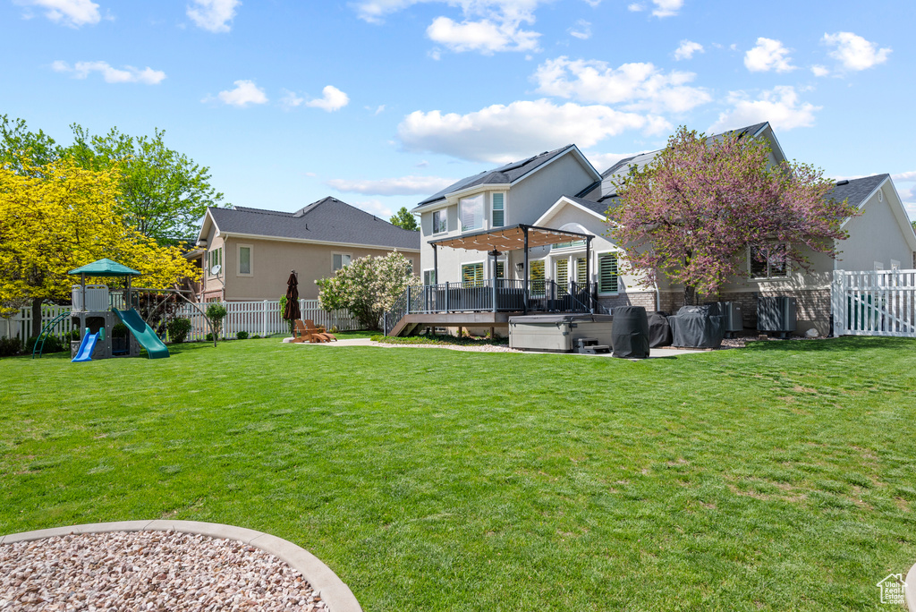 Back of house with a hot tub, a playground, and a wooden deck