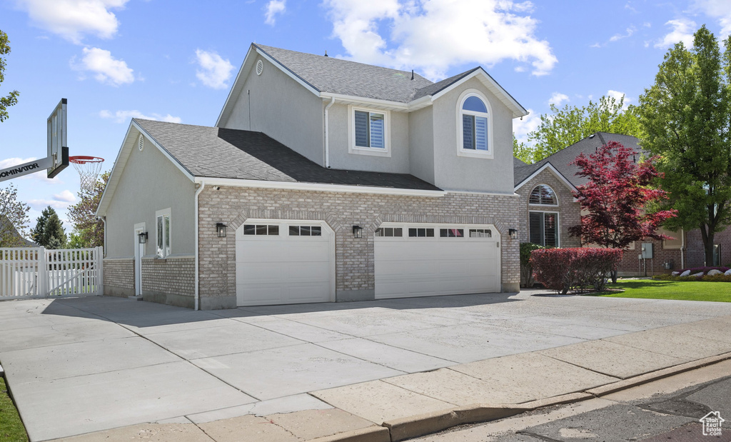 Traditional home with concrete driveway, brick siding, stucco siding, a garage, and fence