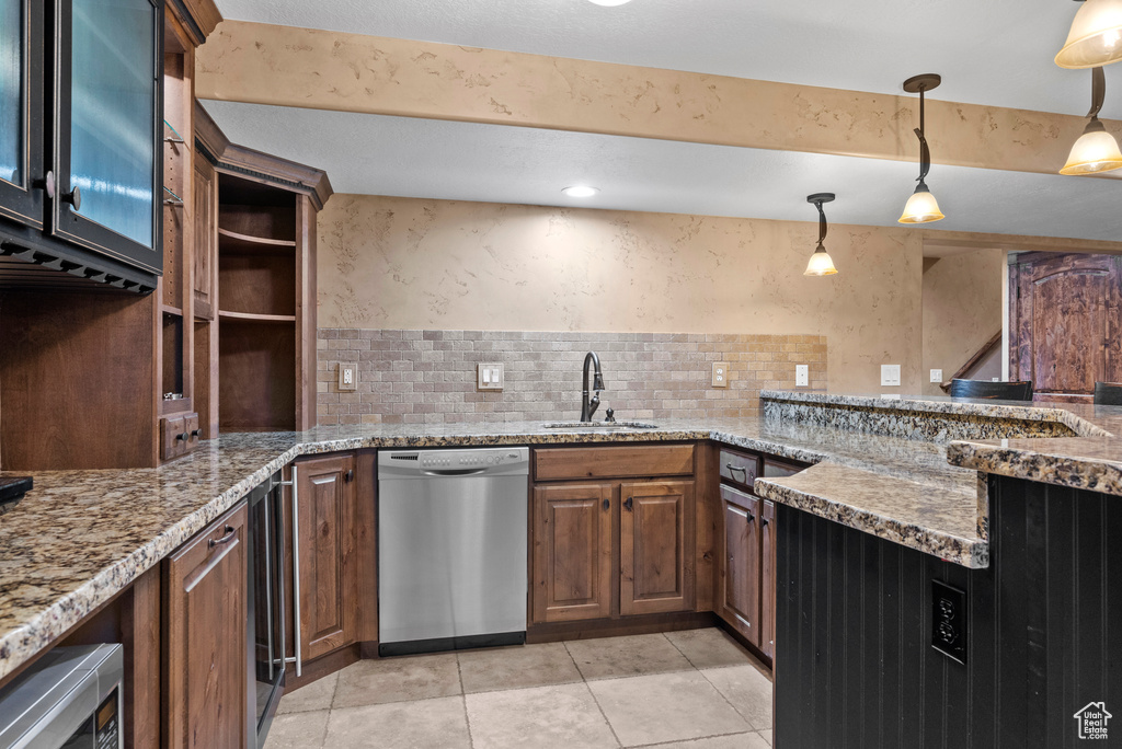 Kitchen with dishwasher, a sink, light stone counters, hanging light fixtures, and light tile patterned floors