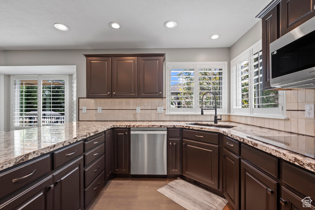 Kitchen with stainless steel appliances, a sink, dark brown cabinets, wood finished floors, and recessed lighting