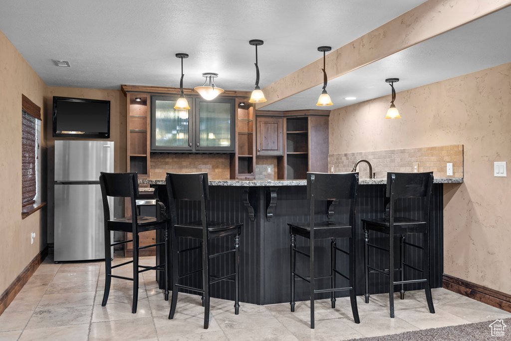 Bar with freestanding refrigerator, baseboards, decorative light fixtures, and a textured wall