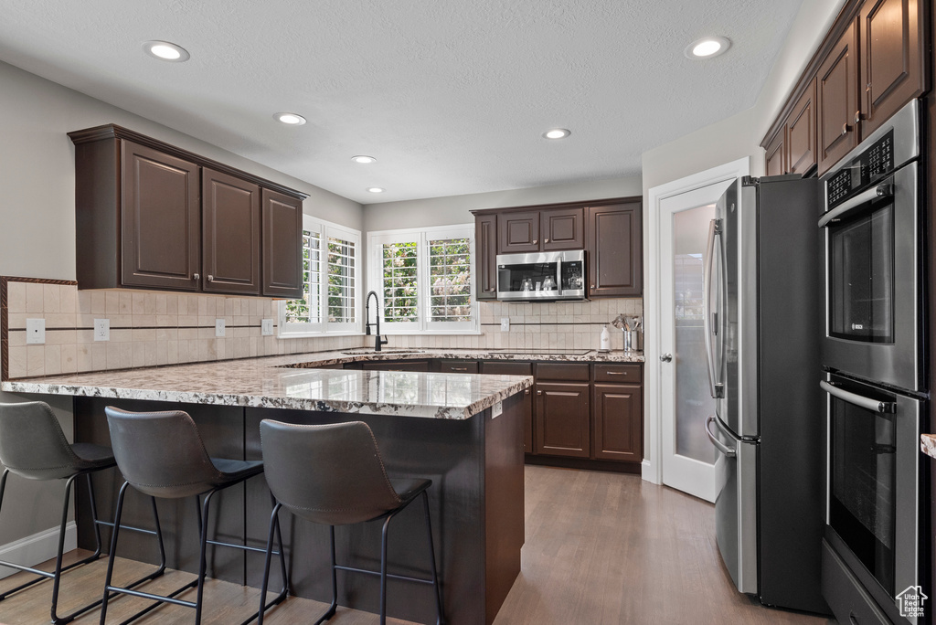 Kitchen featuring stainless steel appliances, a sink, a kitchen breakfast bar, dark wood-style flooring, and dark brown cabinets