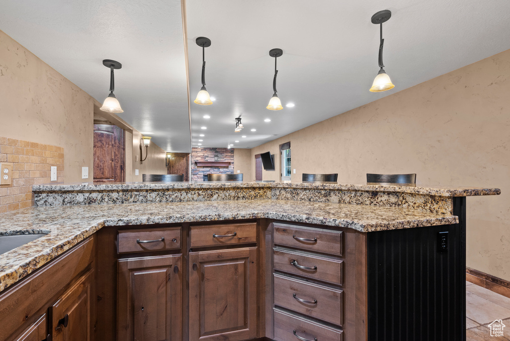 Kitchen with light stone countertops, a peninsula, hanging light fixtures, a fireplace, and open floor plan