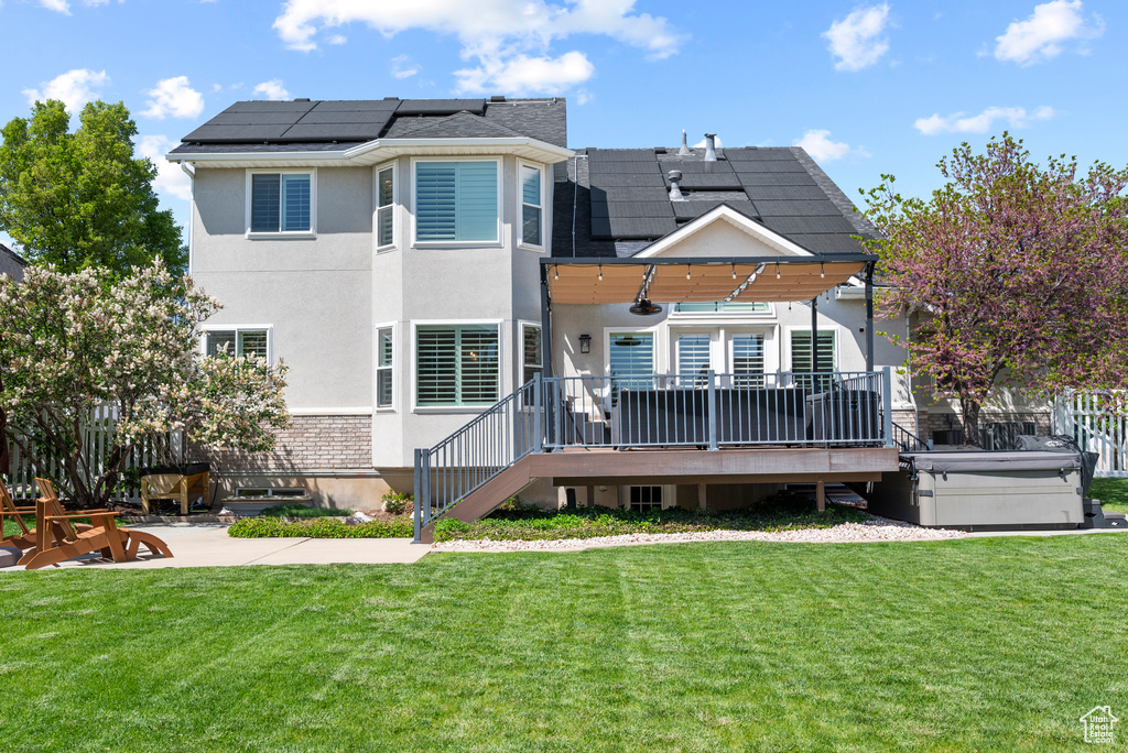 Rear view of house with solar panels, a lawn, a patio, and a deck
