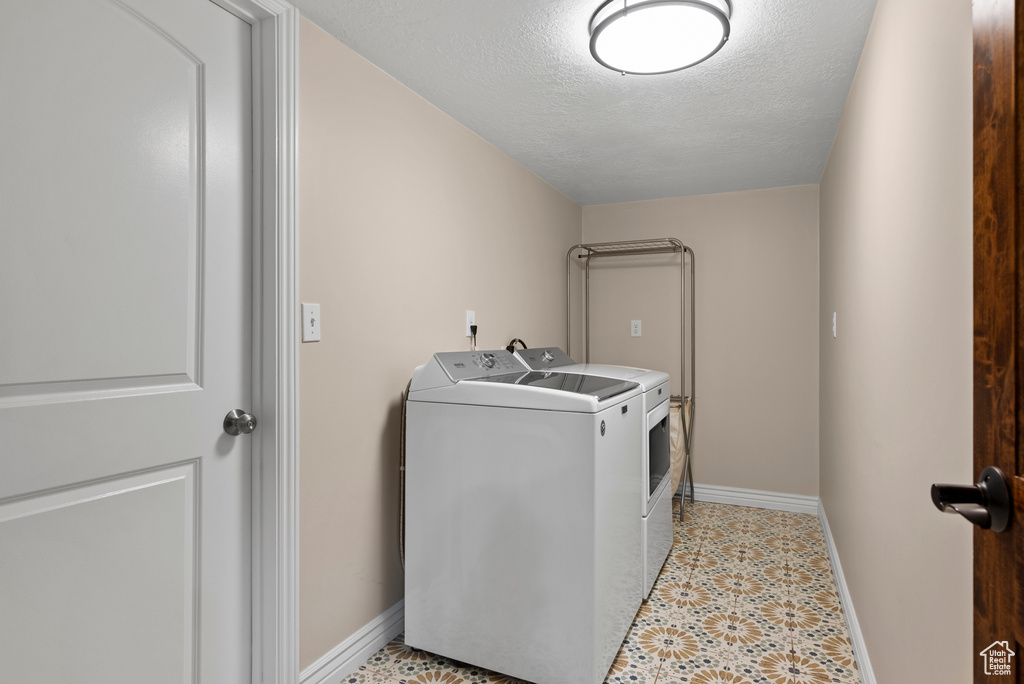 Clothes washing area featuring washer and dryer, baseboards, and a textured ceiling
