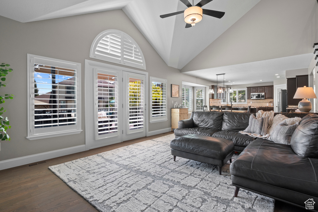 Living area with a ceiling fan, wood finished floors, baseboards, high vaulted ceiling, and a chandelier