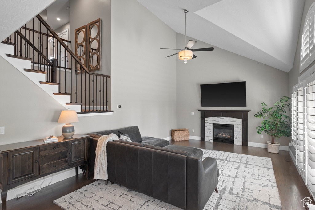 Living room featuring high vaulted ceiling, wood finished floors, a ceiling fan, stairs, and a glass covered fireplace