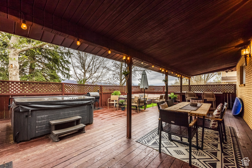 Wooden terrace with outdoor dining area, a hot tub, and a fenced backyard