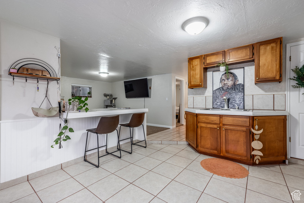 Kitchen with a sink, light countertops, brown cabinets, a textured ceiling, and a peninsula