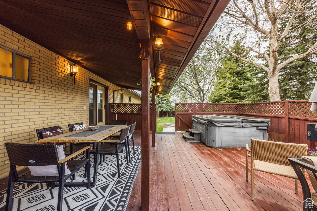 Wooden terrace featuring a hot tub, outdoor dining area, and a fenced backyard