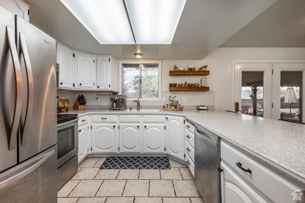 Kitchen featuring stainless steel appliances, a sink, light tile patterned floors, backsplash, and healthy amount of natural light