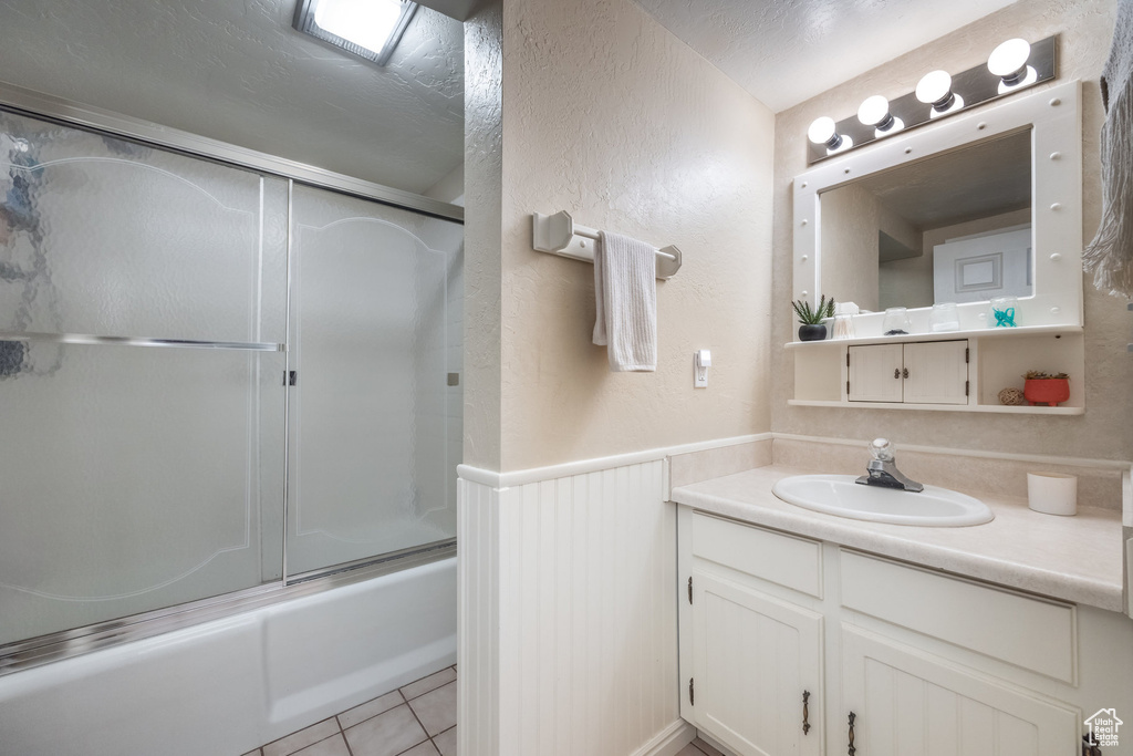 Full bathroom with a wainscoted wall, vanity, shower / bath combination with glass door, tile patterned floors, and a textured wall