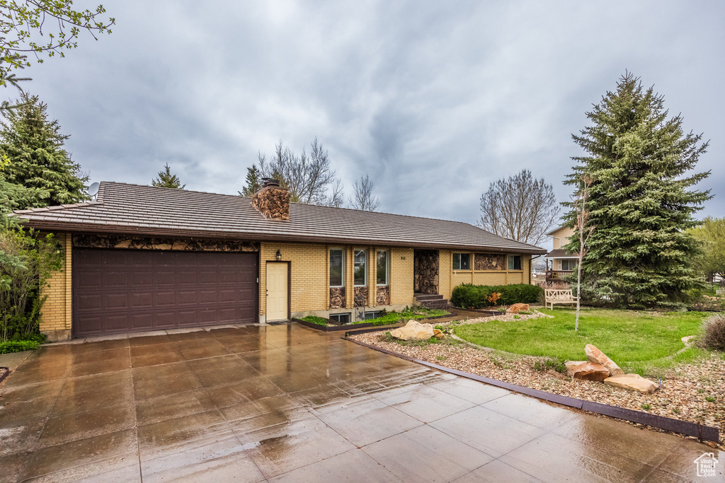Ranch-style home with brick siding, a garage, a chimney, a front lawn, and a tiled roof
