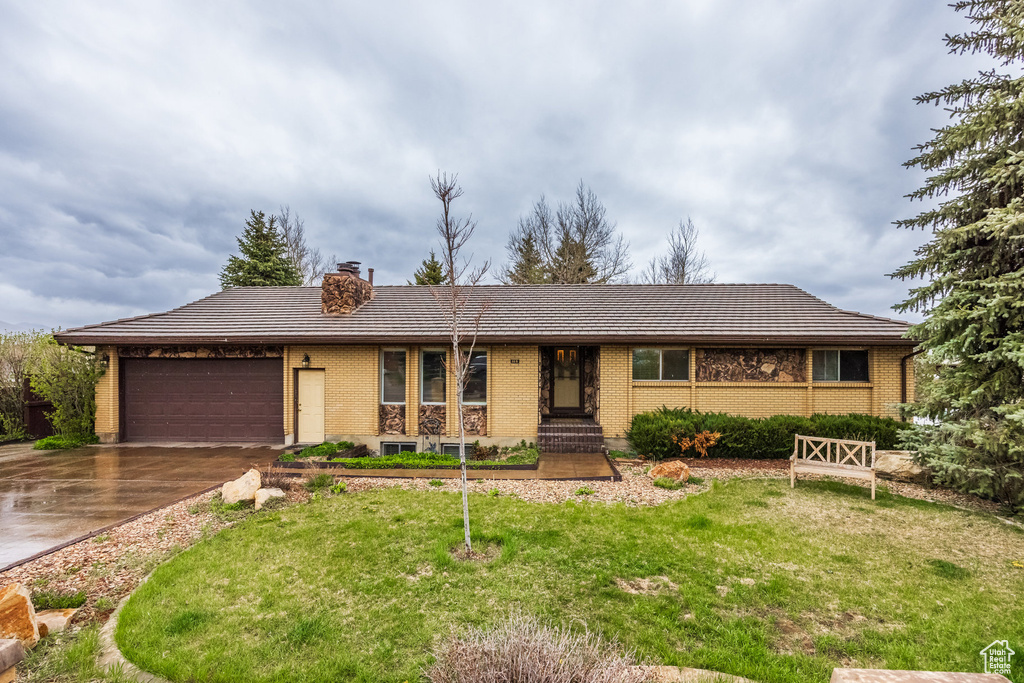 Ranch-style home featuring an attached garage, a chimney, a front yard, and concrete driveway