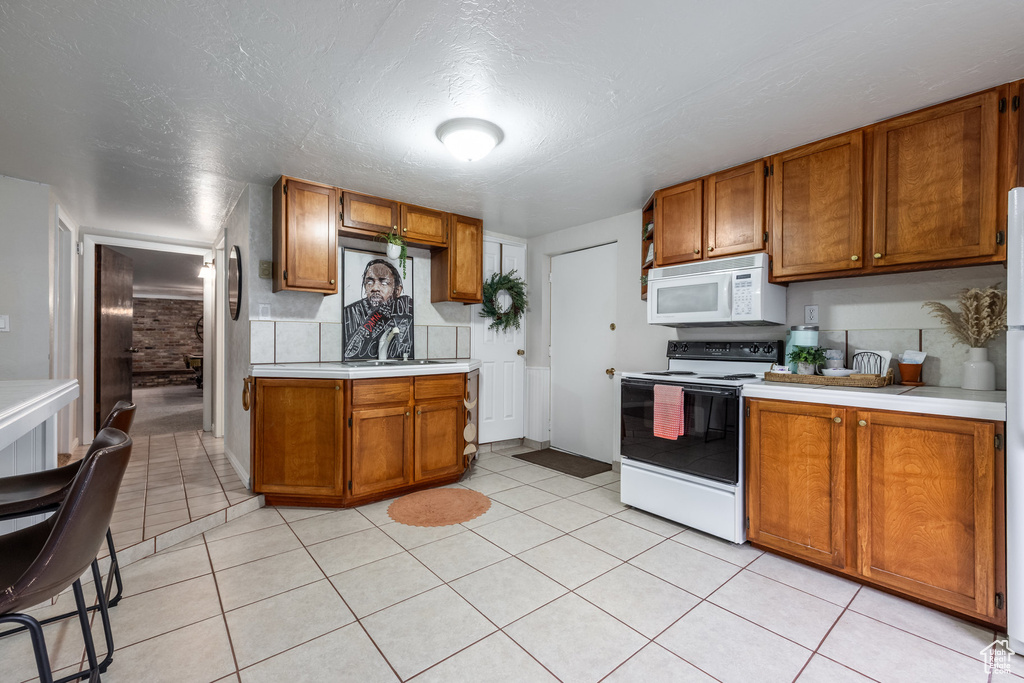 Kitchen featuring electric stove, white microwave, light countertops, and brown cabinets