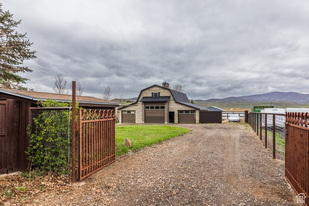 View of front facade with a garage, fence, a mountain view, dirt driveway, and an outdoor structure