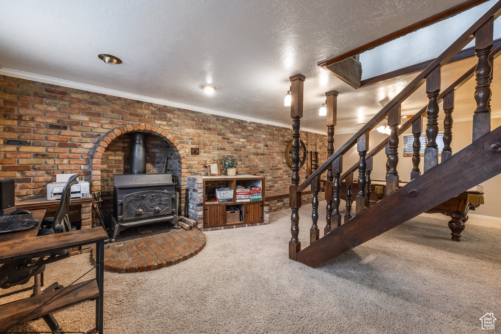 Carpeted living area with a wood stove, ornamental molding, stairs, a textured ceiling, and brick wall