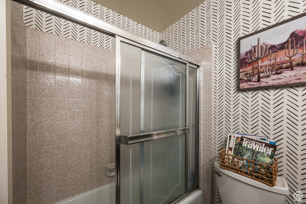Full bathroom featuring shower / bath combination with glass door, toilet, and tile walls