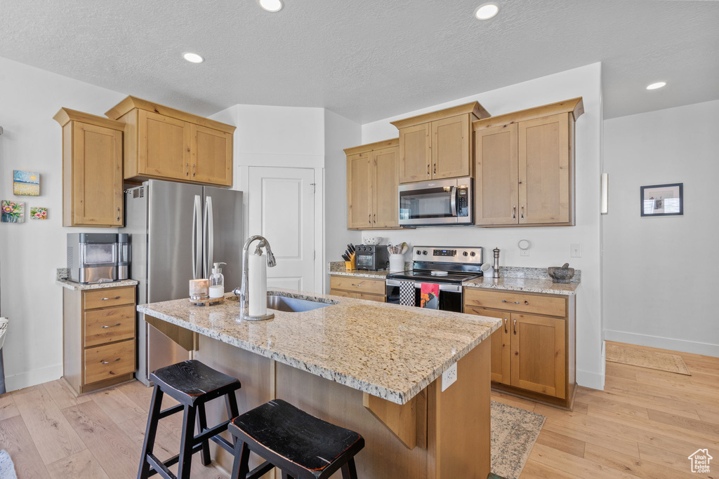 Kitchen featuring appliances with stainless steel finishes, a sink, baseboards, a kitchen island with sink, and light stone countertops