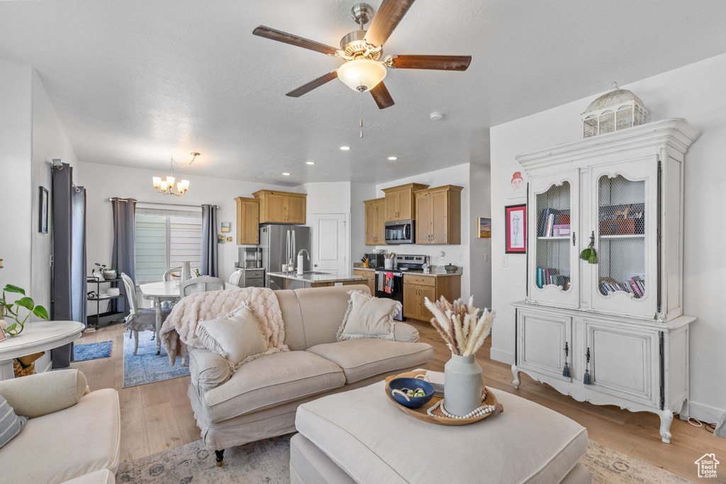 Living room featuring a chandelier, light wood-type flooring, a ceiling fan, and recessed lighting