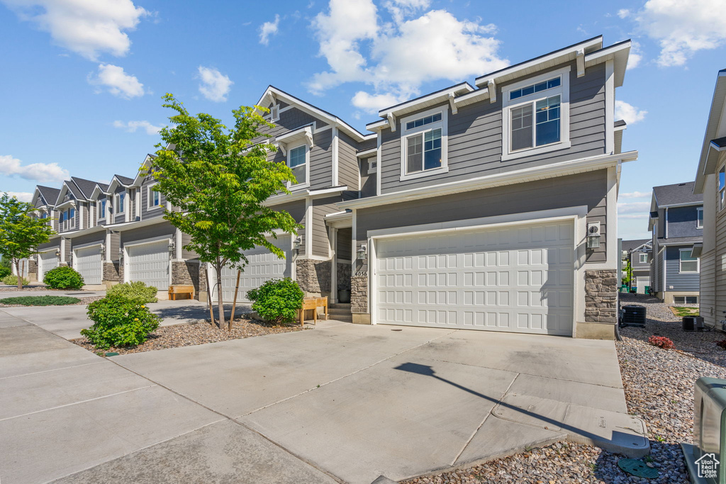 View of front of home featuring stone siding, a garage, concrete driveway, and a residential view