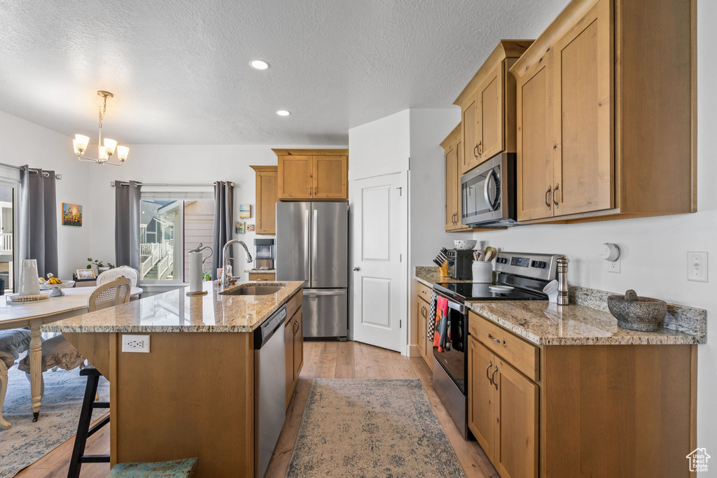 Kitchen featuring appliances with stainless steel finishes, a sink, a chandelier, light wood-type flooring, and a textured ceiling