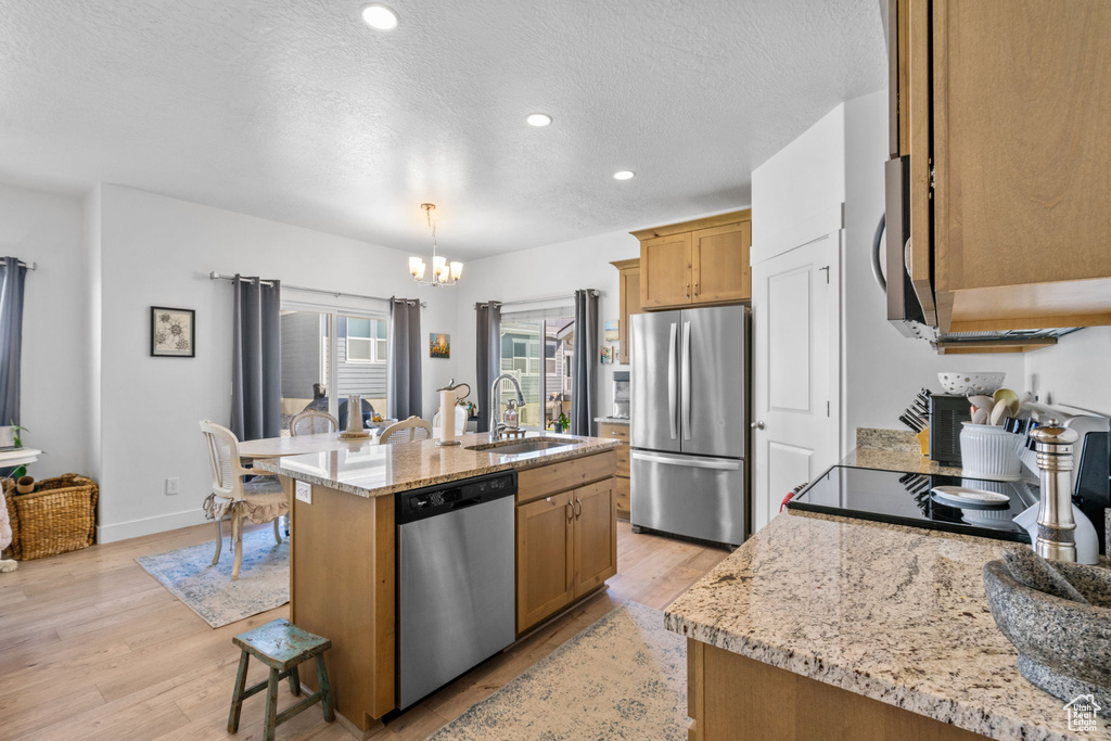 Kitchen featuring appliances with stainless steel finishes, a sink, a chandelier, light wood-style flooring, and a center island with sink