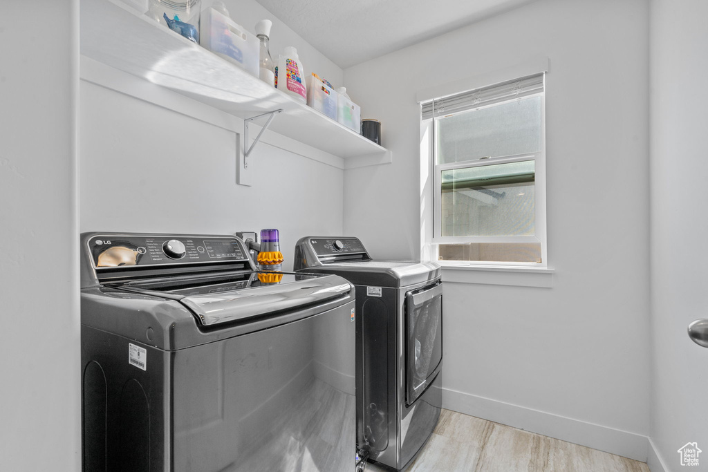 Laundry area with washer and clothes dryer, baseboards, and light wood-style flooring