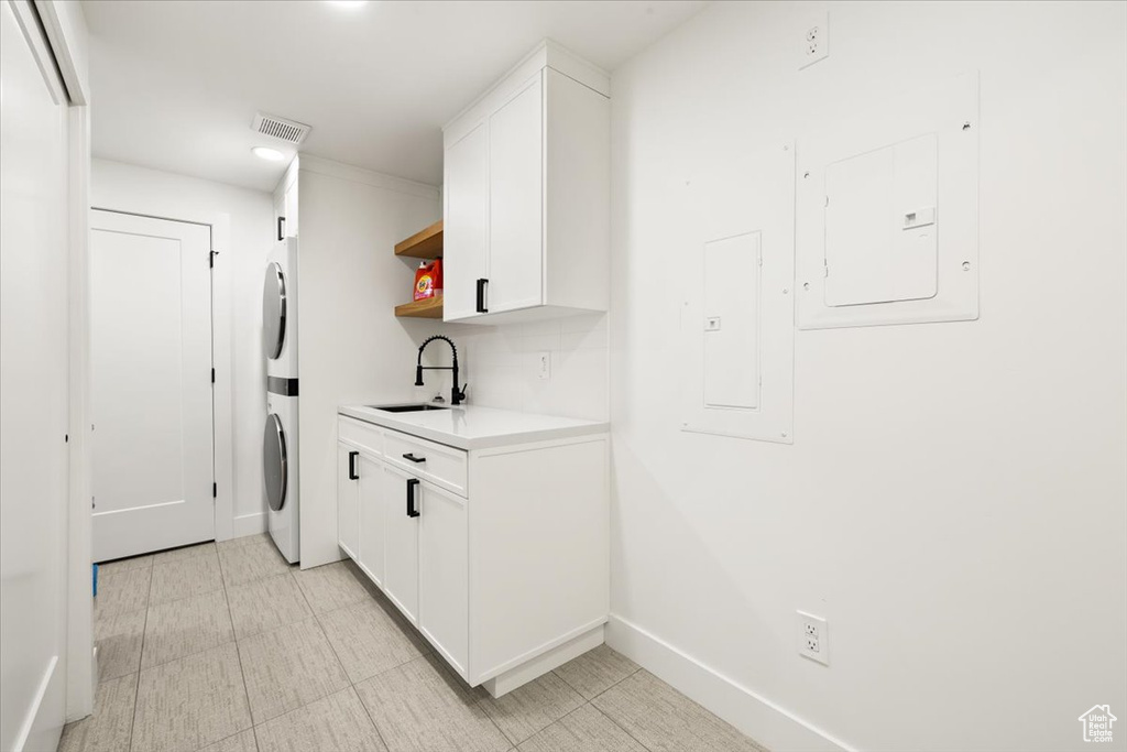 Clothes washing area with stacked washer / dryer, a sink, baseboards, recessed lighting, and light flooring
