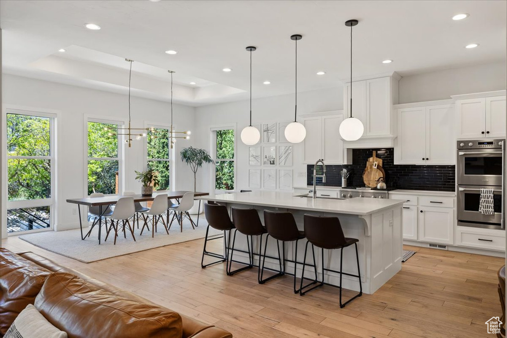 Kitchen featuring double oven, a tray ceiling, backsplash, healthy amount of natural light, and recessed lighting