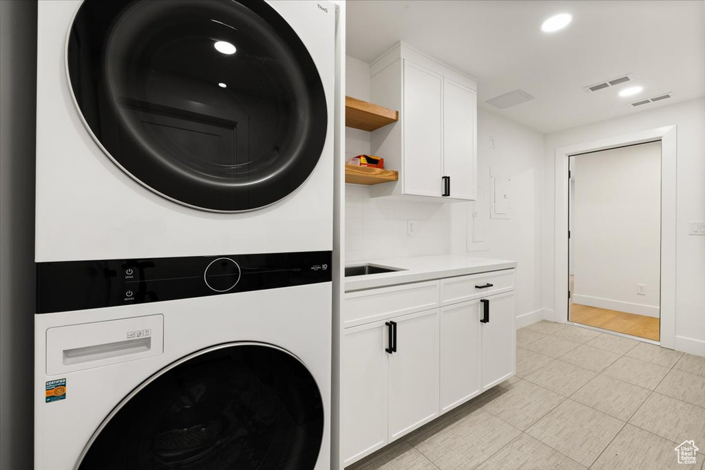 Laundry area featuring stacked washer / dryer, cabinet space, baseboards, and recessed lighting