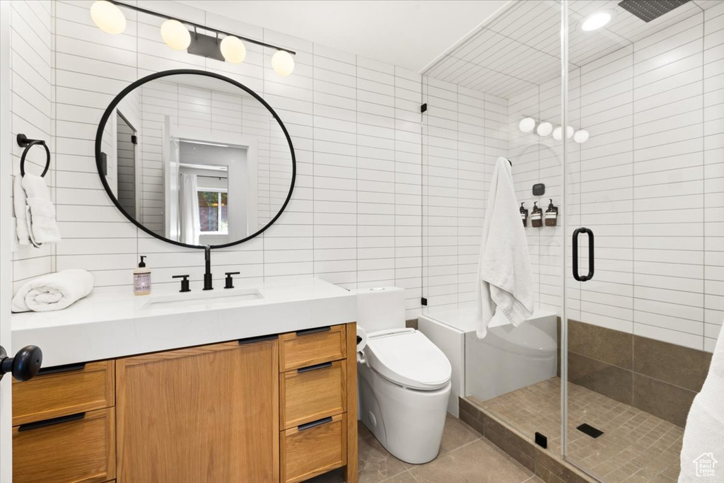 Bathroom with a tile shower, tile walls, tile patterned flooring, vanity, and toilet