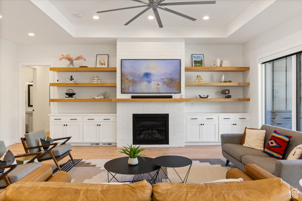 Living room featuring ceiling fan, a fireplace, light wood finished floors, a tray ceiling, and recessed lighting