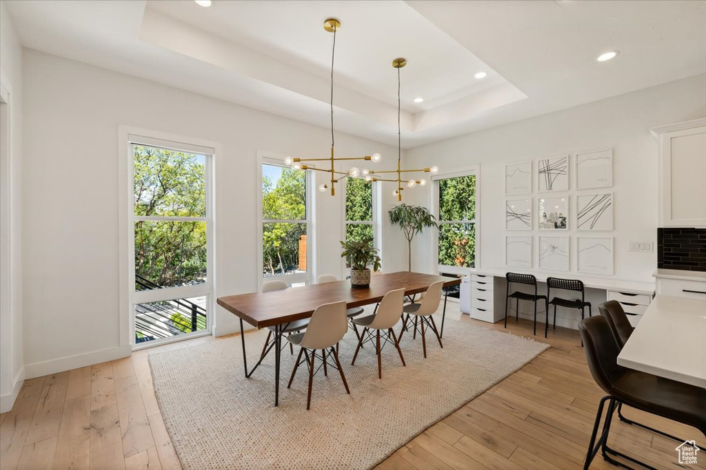 Dining space featuring healthy amount of natural light, a raised ceiling, light wood finished floors, a chandelier, and recessed lighting