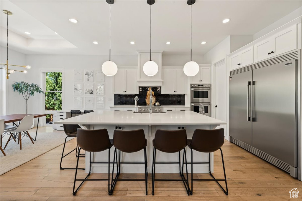 Kitchen featuring appliances with stainless steel finishes, backsplash, light countertops, light wood-style floors, and white cabinets