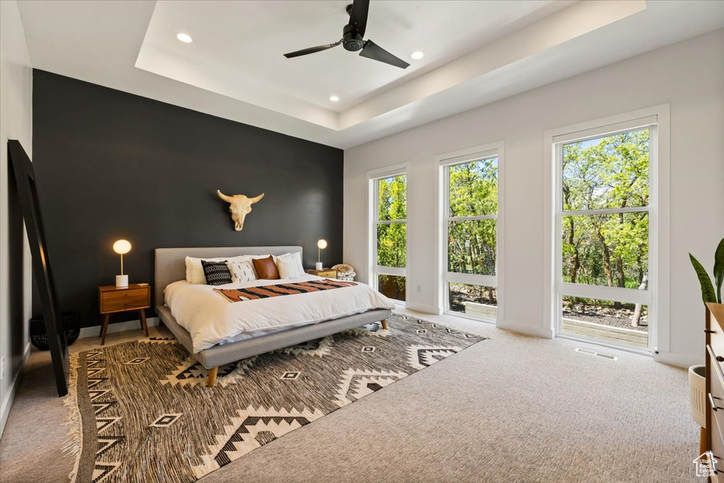 Carpeted bedroom featuring recessed lighting, an accent wall, a tray ceiling, ceiling fan, and baseboards