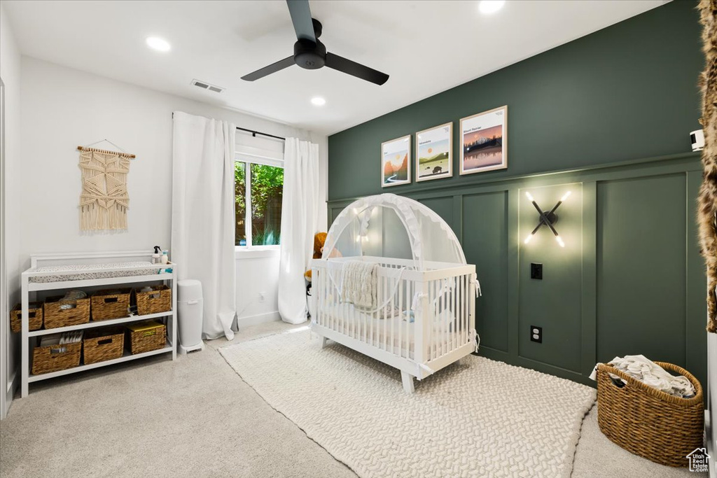 Carpeted bedroom featuring a decorative wall, a nursery area, recessed lighting, ceiling fan, and a wainscoted wall