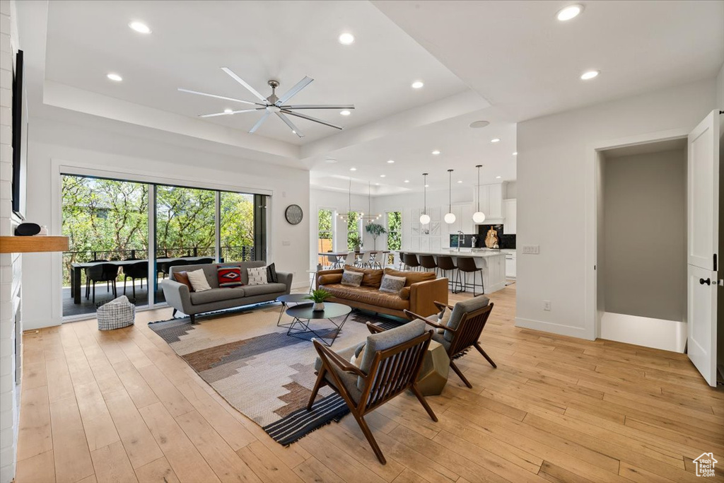 Living room featuring a tray ceiling, recessed lighting, a ceiling fan, light wood-style floors, and baseboards