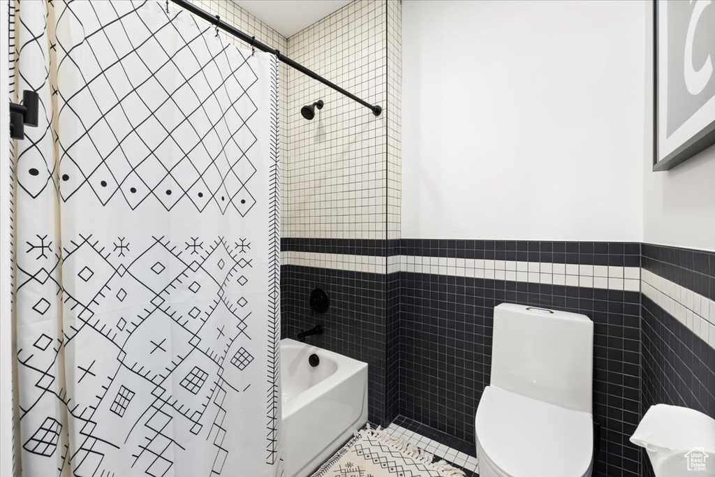 Bathroom with tile walls, shower / bath combination with curtain, toilet, tile patterned flooring, and a wainscoted wall