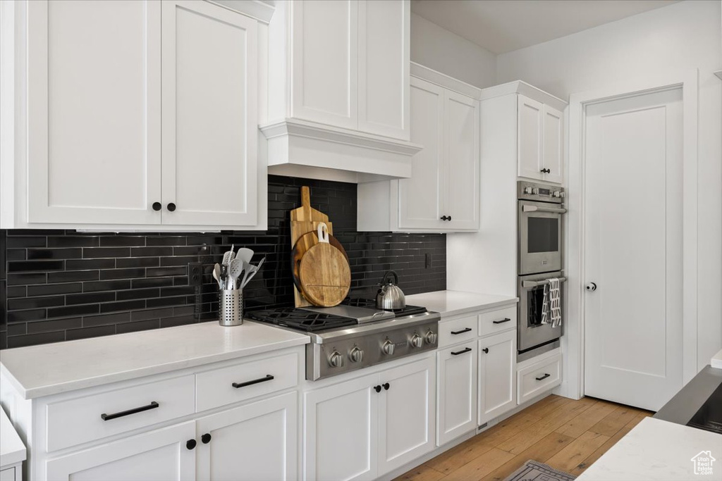 Kitchen featuring stainless steel appliances, white cabinetry, light wood-style flooring, backsplash, and light countertops