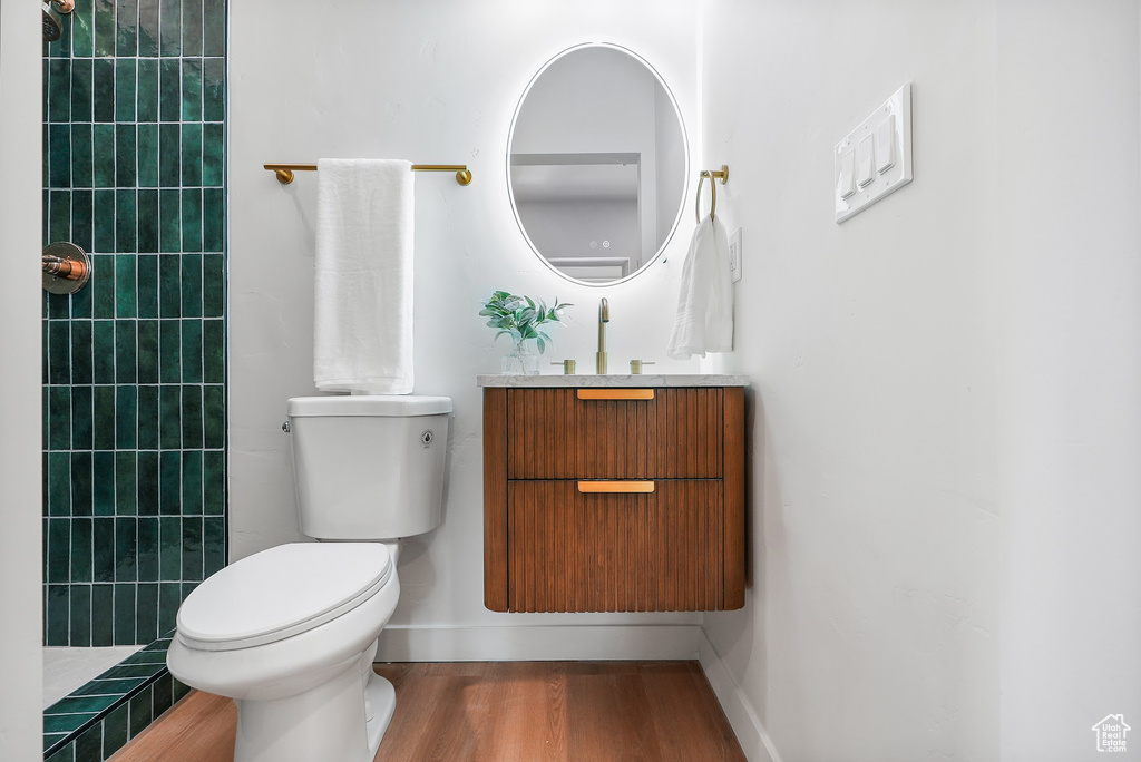 Bathroom with toilet, wood finished floors, vanity, and a tile shower