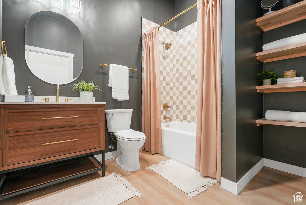 Bathroom featuring wood finished floors, toilet, shower / bath combination with curtain, and vanity