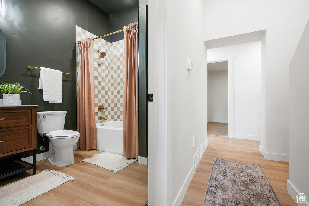 Bathroom featuring wood finished floors, toilet, shower / bathtub combination with curtain, baseboards, and vanity