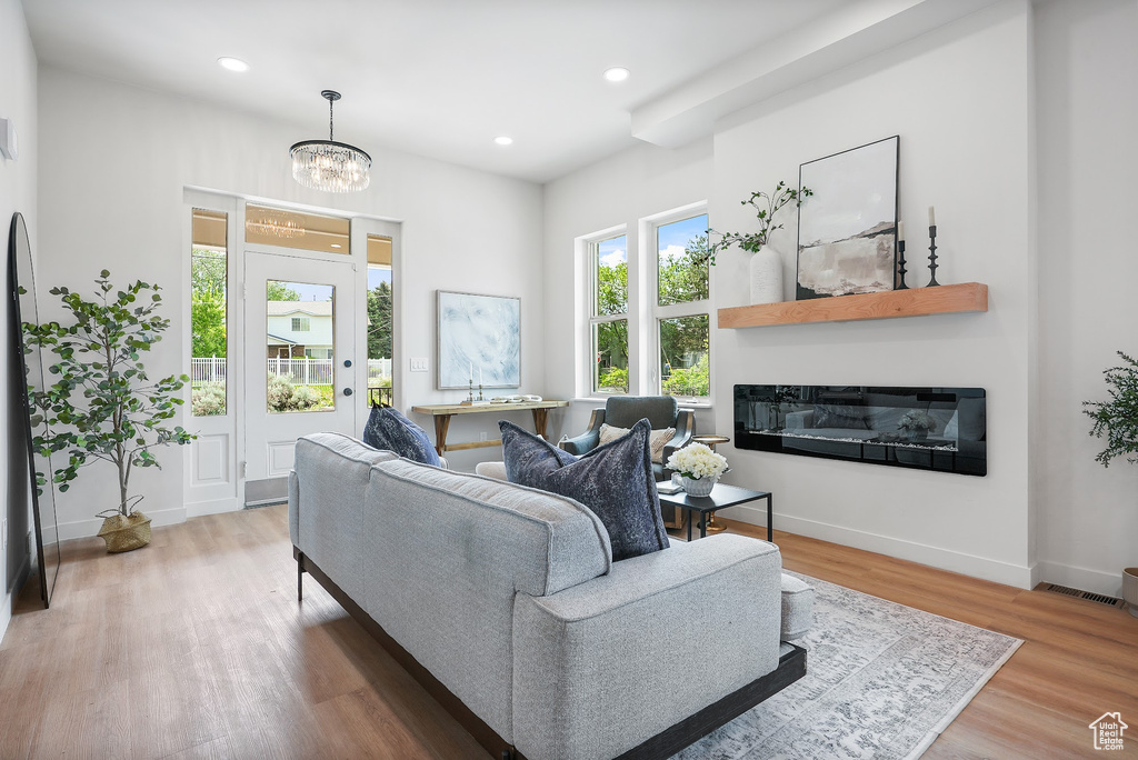 Living area with a glass covered fireplace, wood finished floors, recessed lighting, a chandelier, and baseboards