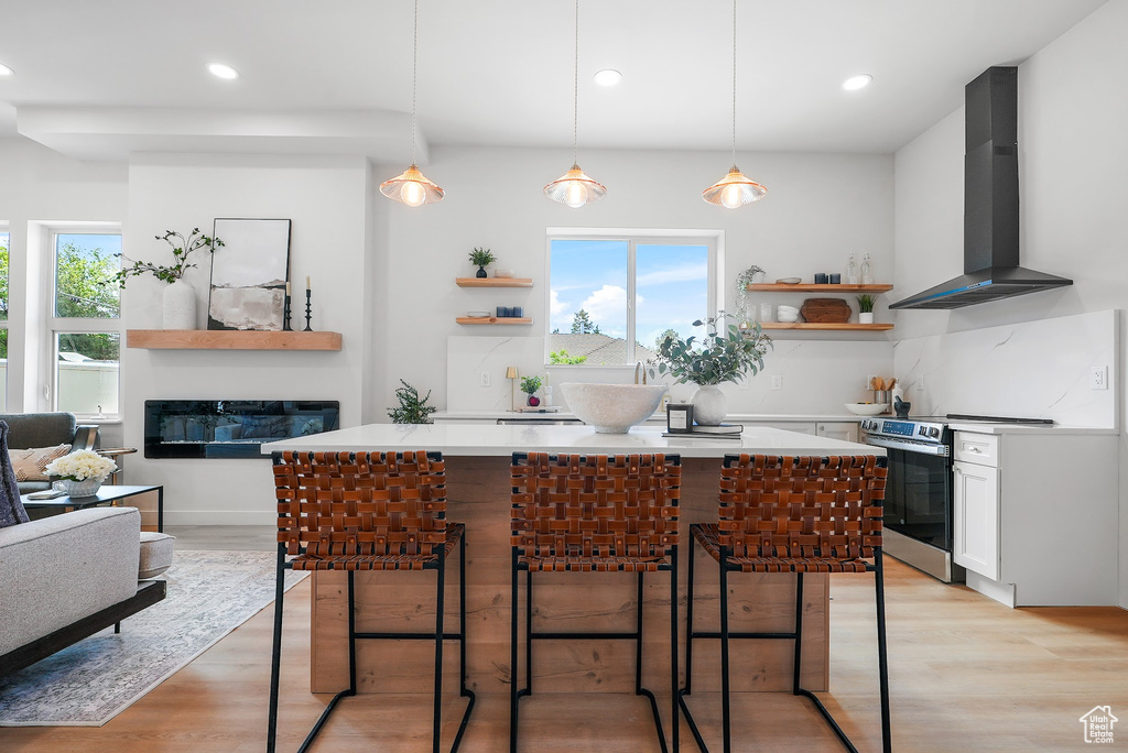 Kitchen with wall chimney range hood, stainless steel electric stove, open shelves, light countertops, and recessed lighting