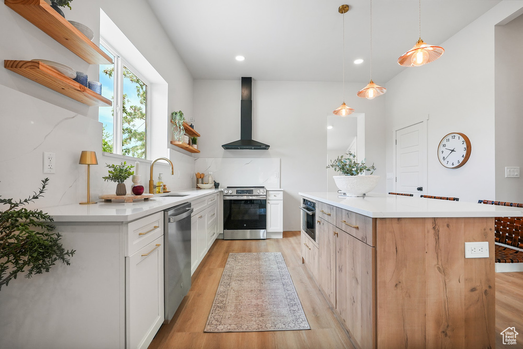 Kitchen featuring open shelves, wall chimney exhaust hood, a sink, appliances with stainless steel finishes, and light wood-style floors