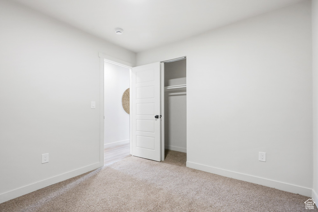 Unfurnished bedroom featuring light carpet, baseboards, and a closet