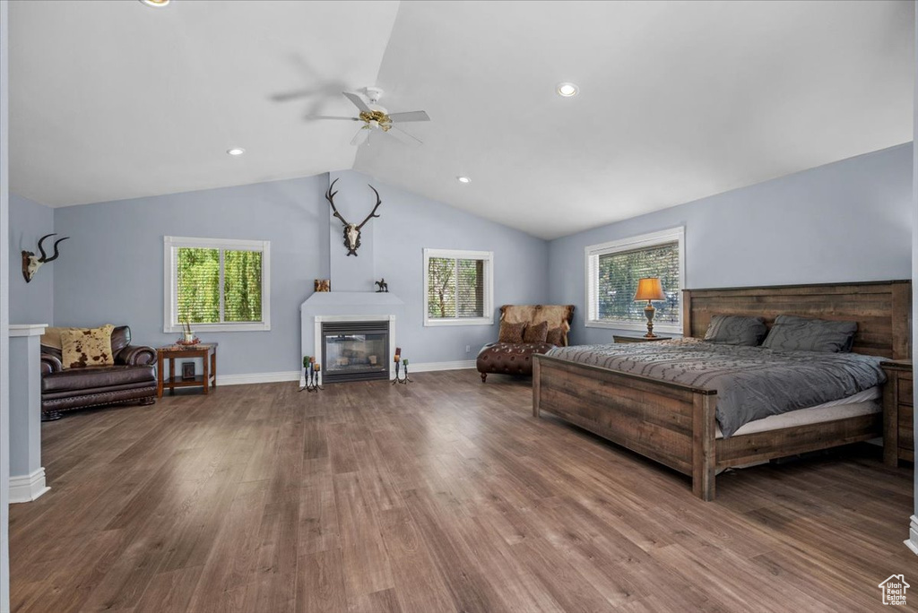 Bedroom featuring a glass covered fireplace, wood finished floors, lofted ceiling, baseboards, and recessed lighting